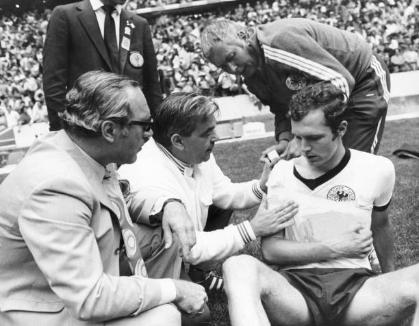 Equipe médica enfaixa o braço de Franz Beckenbauer, tentando simular uma tipoia.
