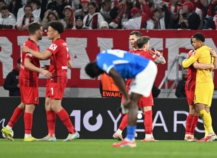 Jogadores do Freiburg comemoram vitória enquanto o Genk reagem tristes após o jogo de volta dos oitavos da UEL. Foto: Thomas Kienzle/AFP.