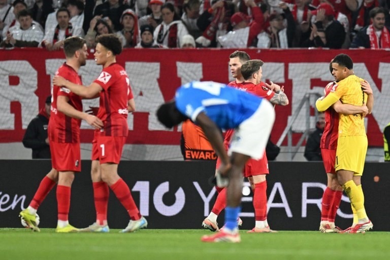 Jogadores do Freiburg comemoram vitória enquanto o Genk reagem tristes após o jogo de volta dos oitavos da UEL. Foto: Thomas Kienzle/AFP.